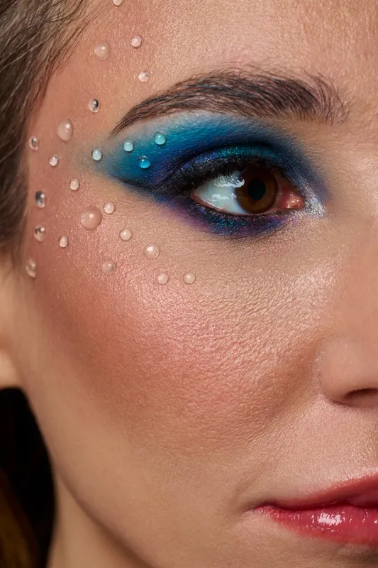 Macro close-up of blue editorial eye makeup with crystal droplets on skin, studio beauty photography Warsaw