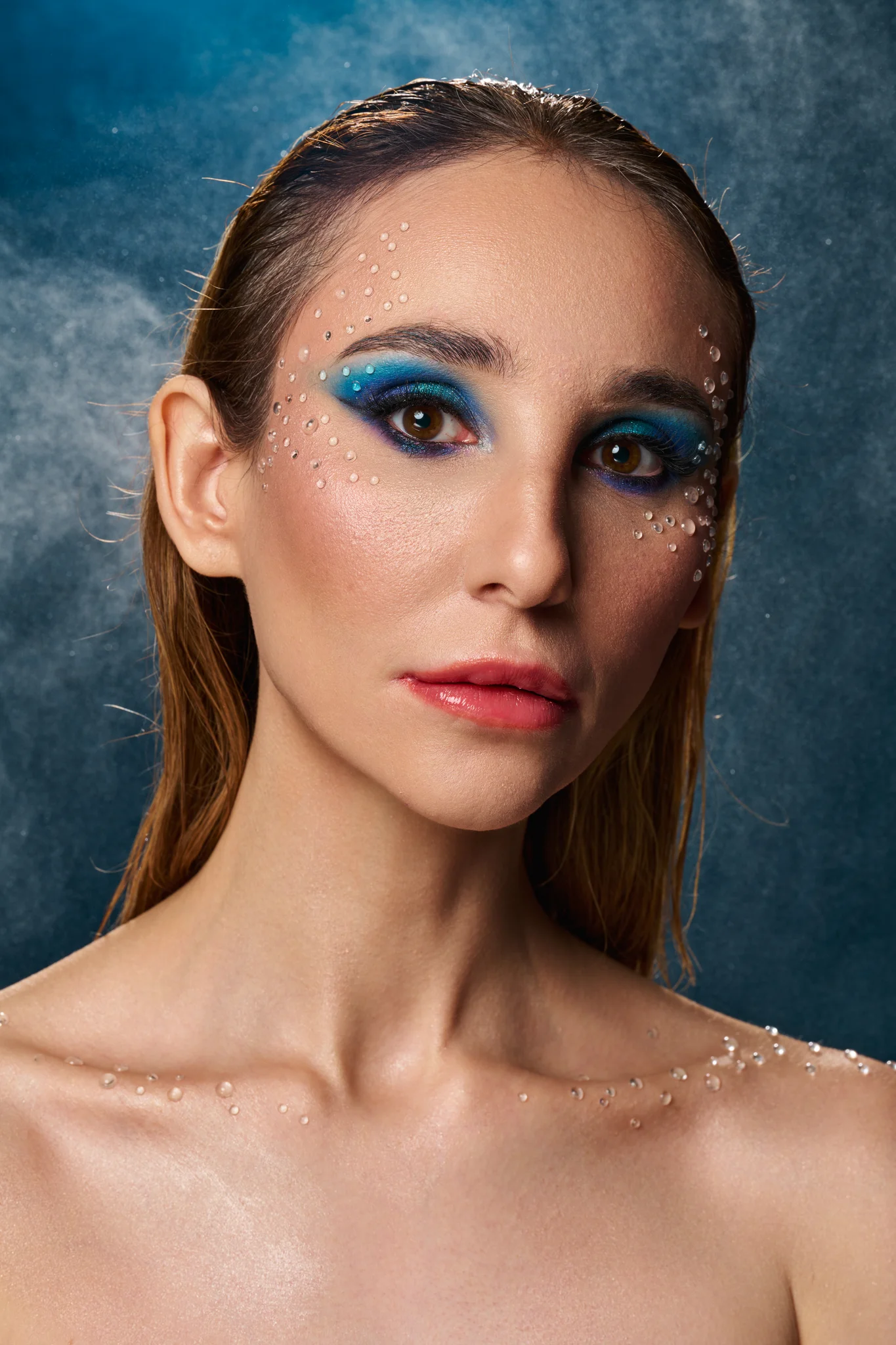 ditorial beauty portrait with blue eyeshadow and crystal droplets, water mist backdrop, direct eye contact