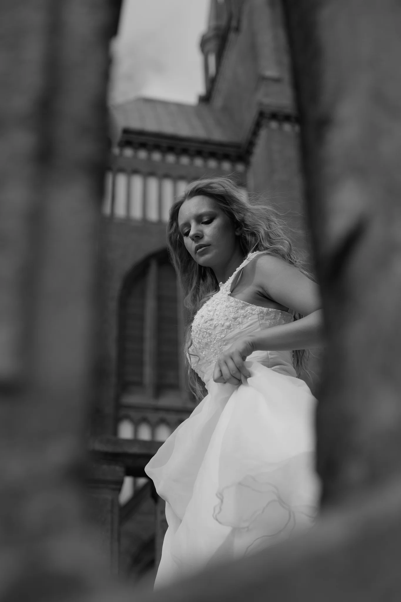 Portrait of woman in wedding dress framed through stone church architecture, eyes closed, black and white outdoor portrait.