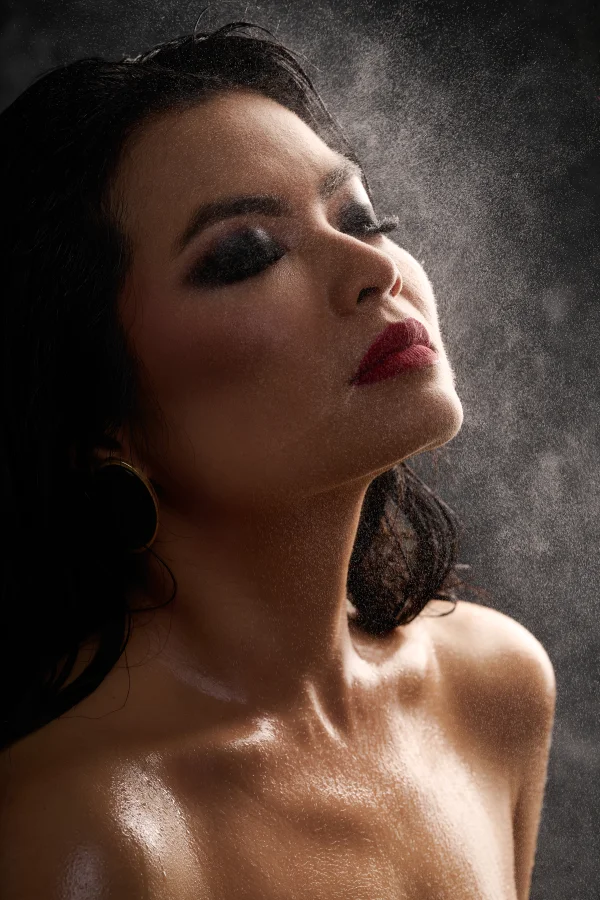 Beauty portrait of model Dii in a wet look, with smokey eye makeup, glowing wet skin, and sprayed water highlighted by the light.