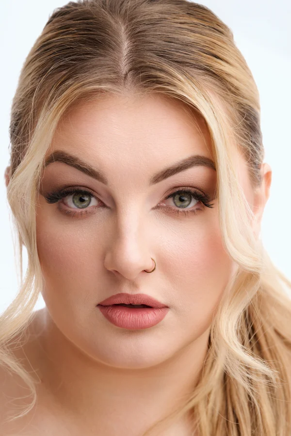 Close-up beauty portrait of a blonde model with professional makeup, photographed on a clean white background using soft Rembrandt lighting.